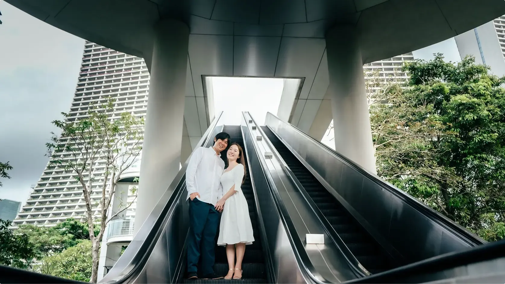 Couple on an escalator framed by concrete columns and the Marina Bay skyline